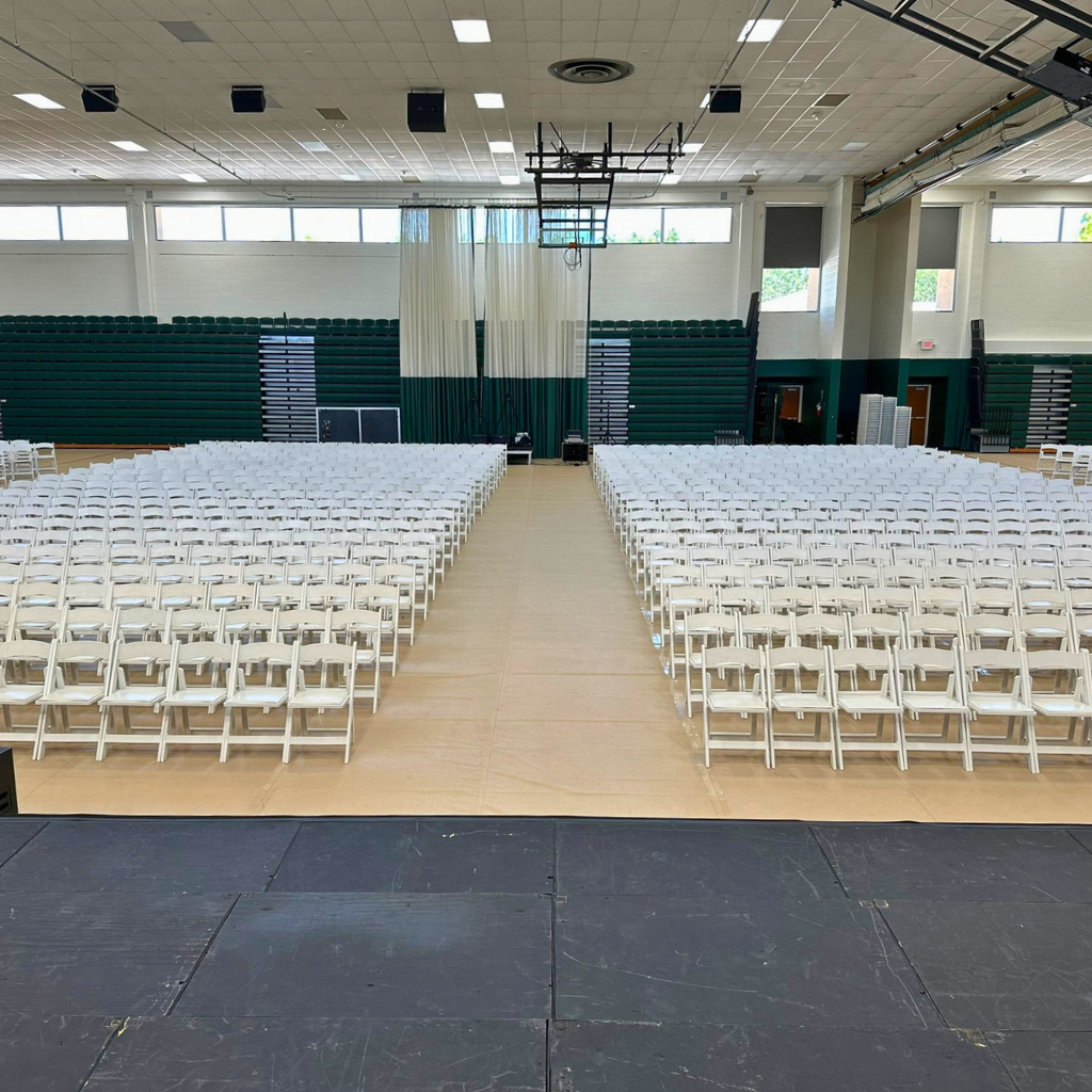 Indoor graduation event setup with stage and audience seating by TLC Event Rentals
